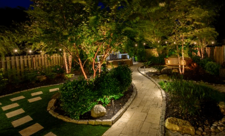 Landscape lighting illuminating a garden walkway, trees, and outdoor path at night